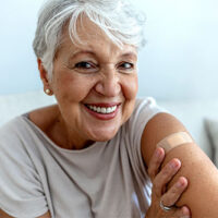 happy older woman showing vaccine spot on arm
