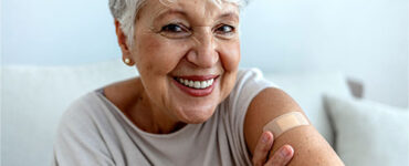 happy older woman showing vaccine spot on arm