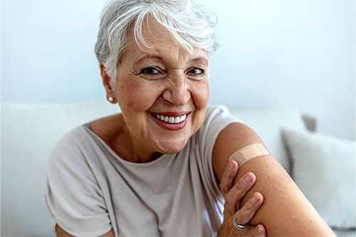 happy older woman showing vaccine spot on arm