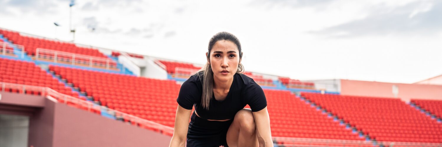 Asian young sportswoman sprint on a running track outdoors on stadium.