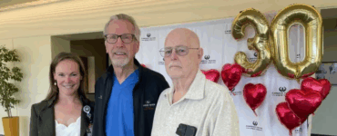Patient stands with members of his care team at Carson Tahoe Health during a heart surgery reunion celebration, with 30th anniversary balloons in the background.