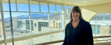 Susanne James stands inside a Carson Tahoe Health facility with large windows overlooking the campus and surrounding mountains.