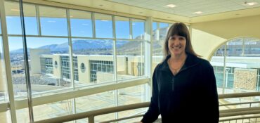 Susanne James stands inside a Carson Tahoe Health facility with large windows overlooking the campus and surrounding mountains.