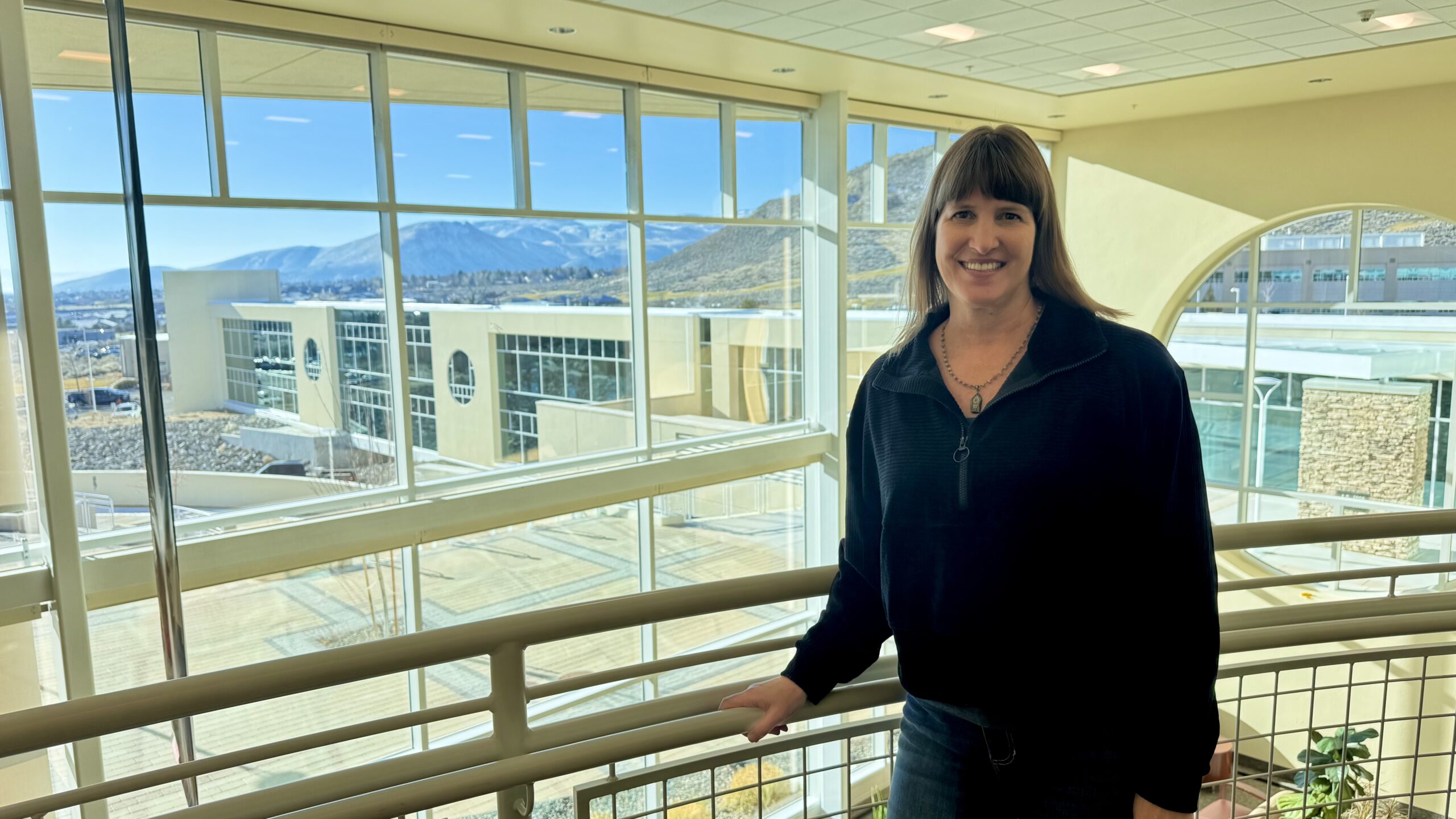 Susanne James stands inside a Carson Tahoe Health facility with large windows overlooking the campus and surrounding mountains.
