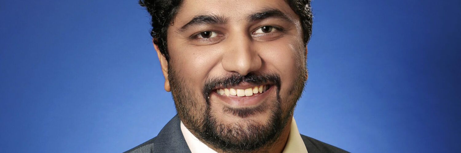 Cardiologist wearing a suit and tie, smiling against a blue studio background