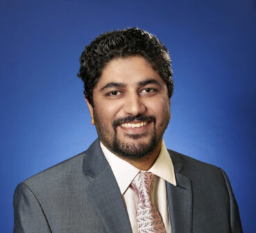 Cardiologist wearing a suit and tie, smiling against a blue studio background
