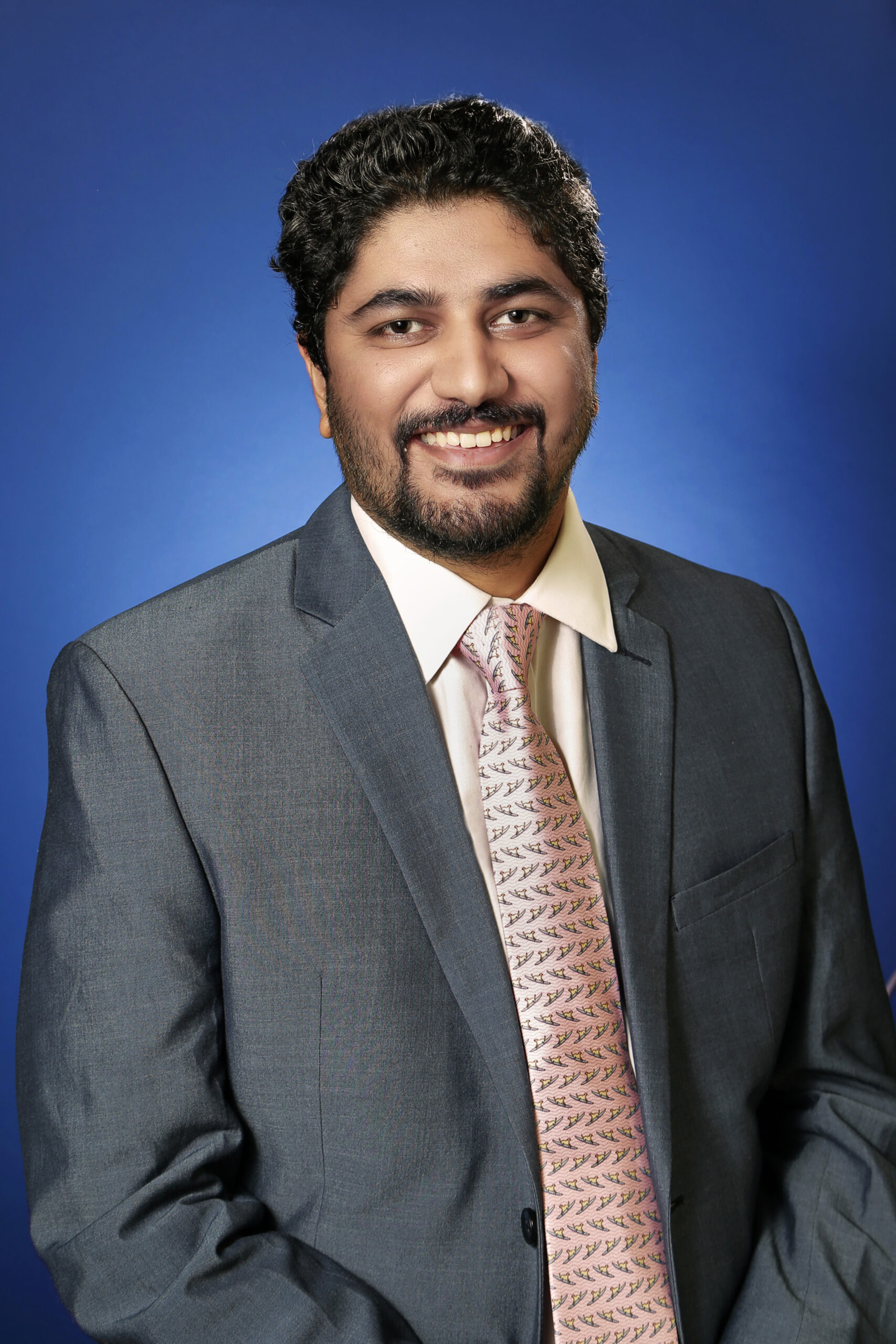 Cardiologist wearing a suit and tie, smiling against a blue studio background