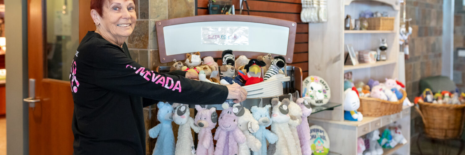 A smiling staff member arranging stuffed animals and baby gifts inside the Carson Tahoe Health Auxiliary Gift Shop.