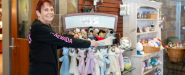 A smiling staff member arranging stuffed animals and baby gifts inside the Carson Tahoe Health Auxiliary Gift Shop.