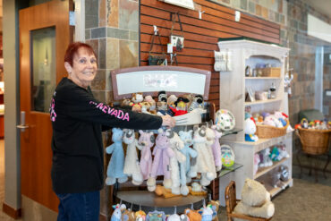 A smiling staff member arranging stuffed animals and baby gifts inside the Carson Tahoe Health Auxiliary Gift Shop.