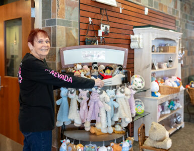 A smiling staff member arranging stuffed animals and baby gifts inside the Carson Tahoe Health Auxiliary Gift Shop.