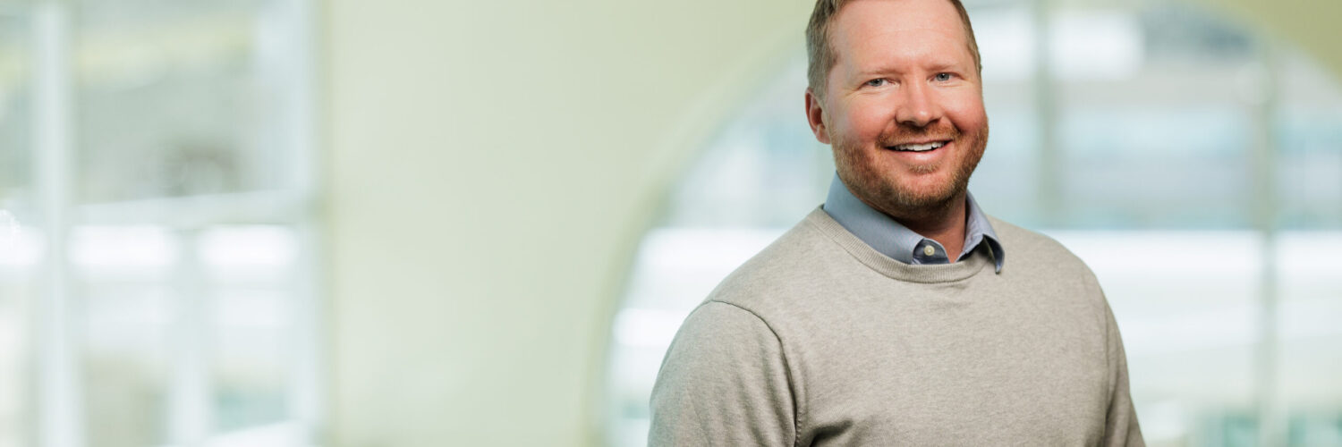 Dylan Linnell, PA-C, standing indoors at Carson Tahoe Health, smiling in a light sweater in a hospital setting.