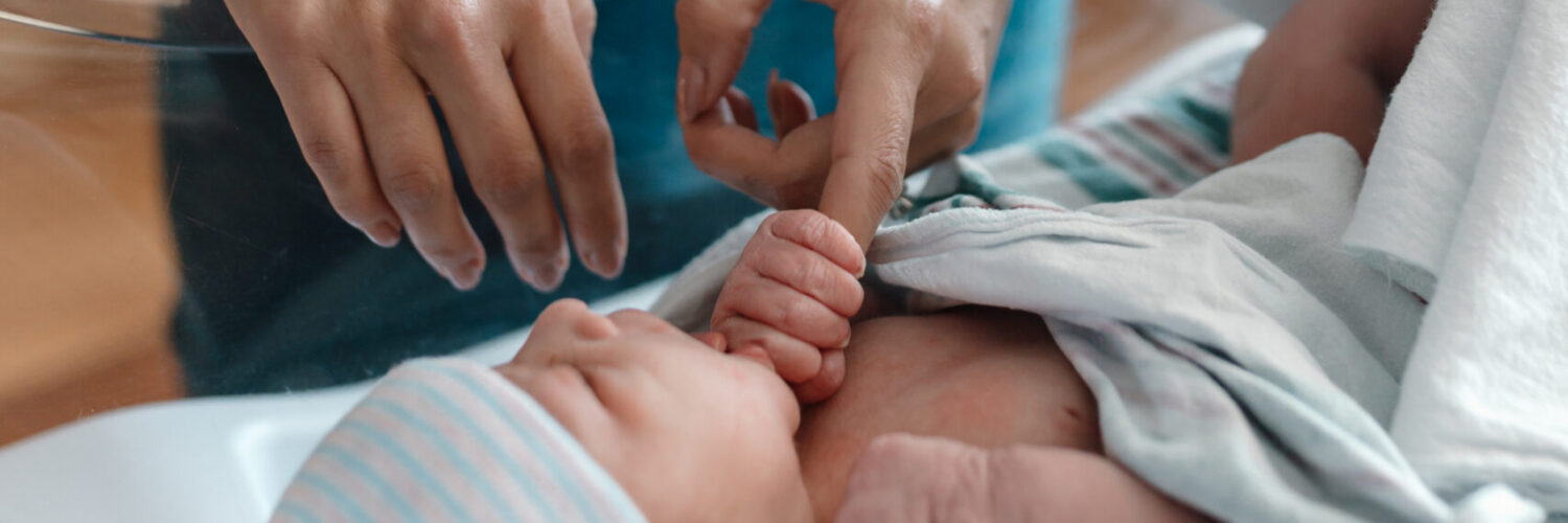 Caregiver in Carson Tahoe Health scrubs gently caring for a newborn baby in a hospital bassinet