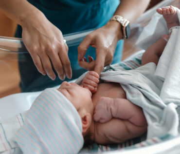 Caregiver in Carson Tahoe Health scrubs gently caring for a newborn baby in a hospital bassinet