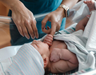 Caregiver in Carson Tahoe Health scrubs gently caring for a newborn baby in a hospital bassinet