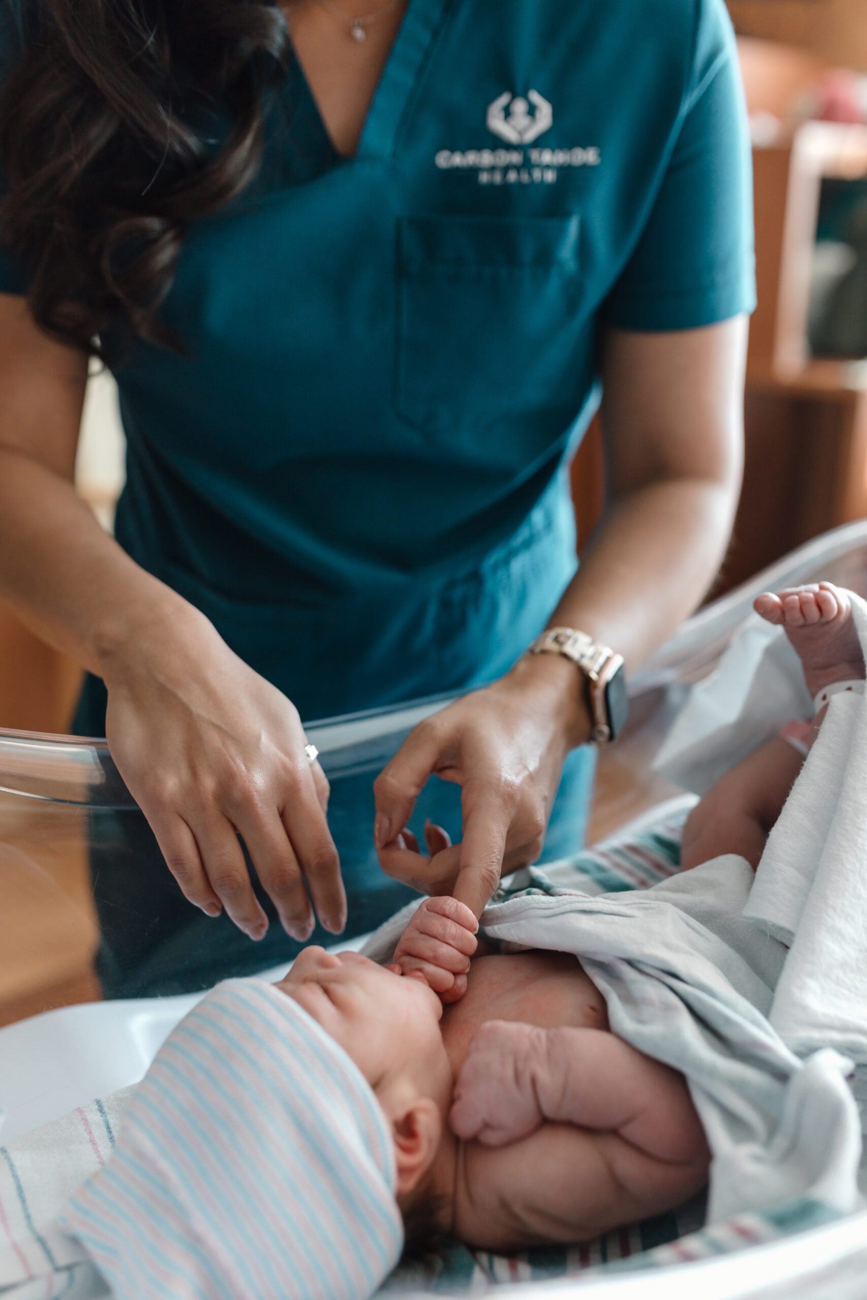 Caregiver in Carson Tahoe Health scrubs gently caring for a newborn baby in a hospital bassinet
