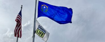 Donate Life flag and U.S. flag raised on flagpoles outside Carson Tahoe Regional Medical Center building under a cloudy sky.