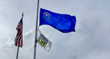 Donate Life flag and U.S. flag raised on flagpoles outside Carson Tahoe Regional Medical Center building under a cloudy sky.