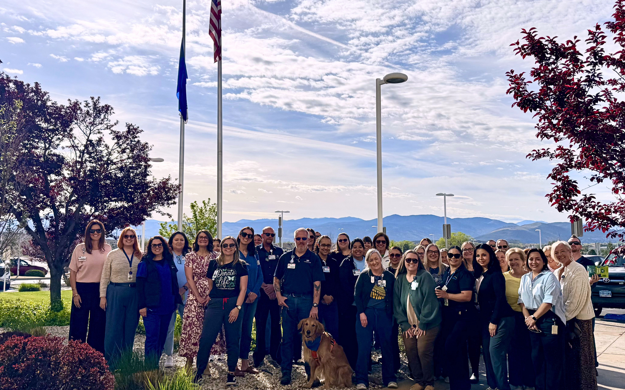 Group of Carson Tahoe Health staff and community members gathered outdoors near a flagpole during a Donate Life flag-raising event, with mountains in the background.