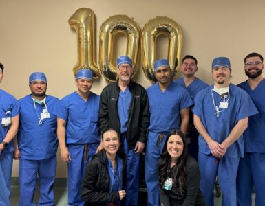 Carson Tahoe Health cardiovascular team celebrating 100th TAVR procedure milestone with staff standing in scrubs in front of gold 100 balloons