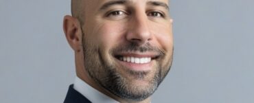 Portrait of Dr. Tabaac smiling in a suit against a neutral background