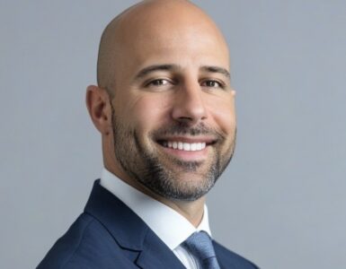 Portrait of Dr. Tabaac smiling in a suit against a neutral background