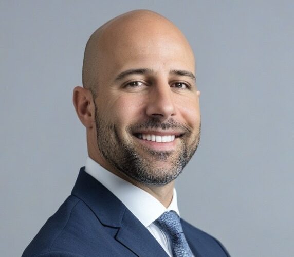 Portrait of Dr. Tabaac smiling in a suit against a neutral background