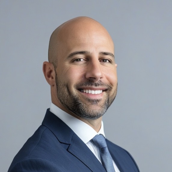 Portrait of Dr. Tabaac smiling in a suit against a neutral background