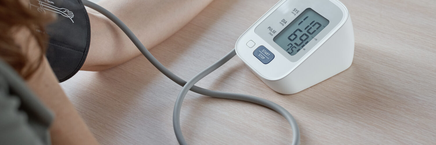 Person measuring blood pressure at home using a digital monitor, showing a reading of 110/69 on the screen.
