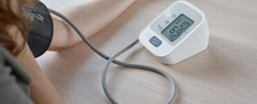 Person measuring blood pressure at home using a digital monitor, showing a reading of 110/69 on the screen.