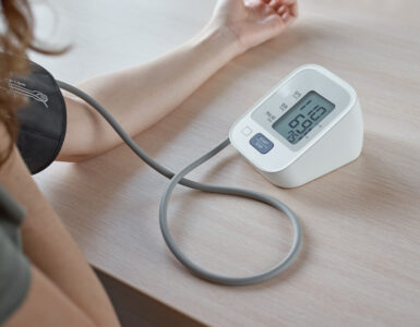 Person measuring blood pressure at home using a digital monitor, showing a reading of 110/69 on the screen.