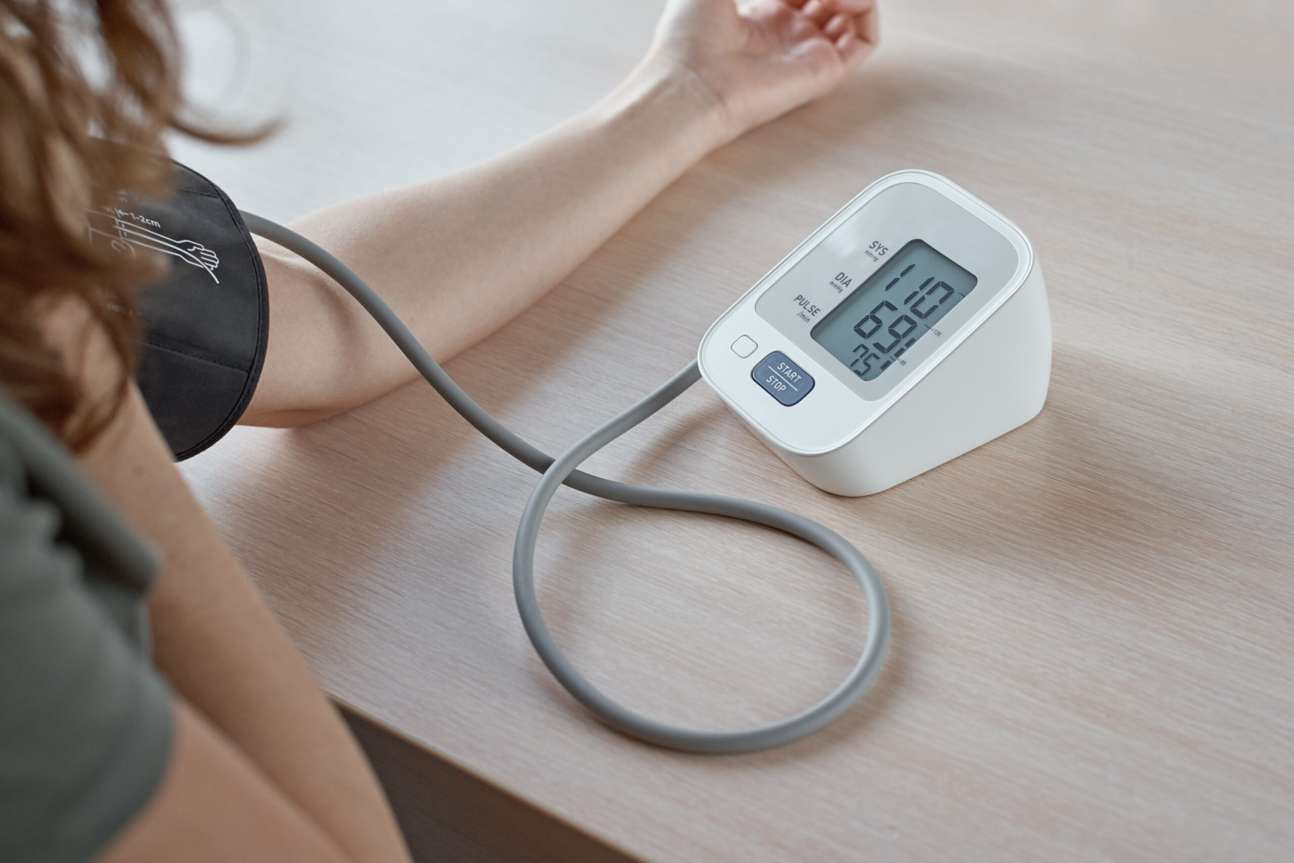Person measuring blood pressure at home using a digital monitor, showing a reading of 110/69 on the screen.