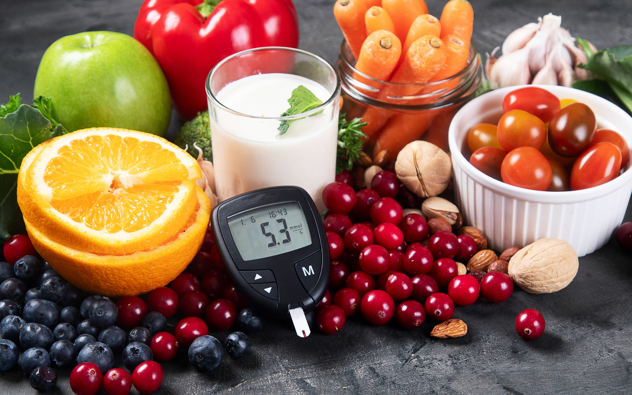 Healthy foods including fruits, vegetables, nuts, and milk with a glucose meter showing blood sugar levels, representing diabetes prevention and healthy lifestyle