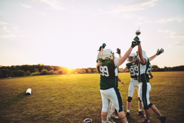 High school football players celebrating on field during practice, representing student athletes preparing for sports season