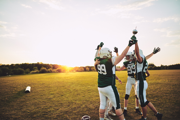 High school football players celebrating on field during practice, representing student athletes preparing for sports season